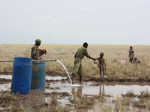 A Kenya Police Reservist delivers clean water to a thirsty child at the Lotikipi Borehole.: Photograph © UNESCO/Nairobi Office